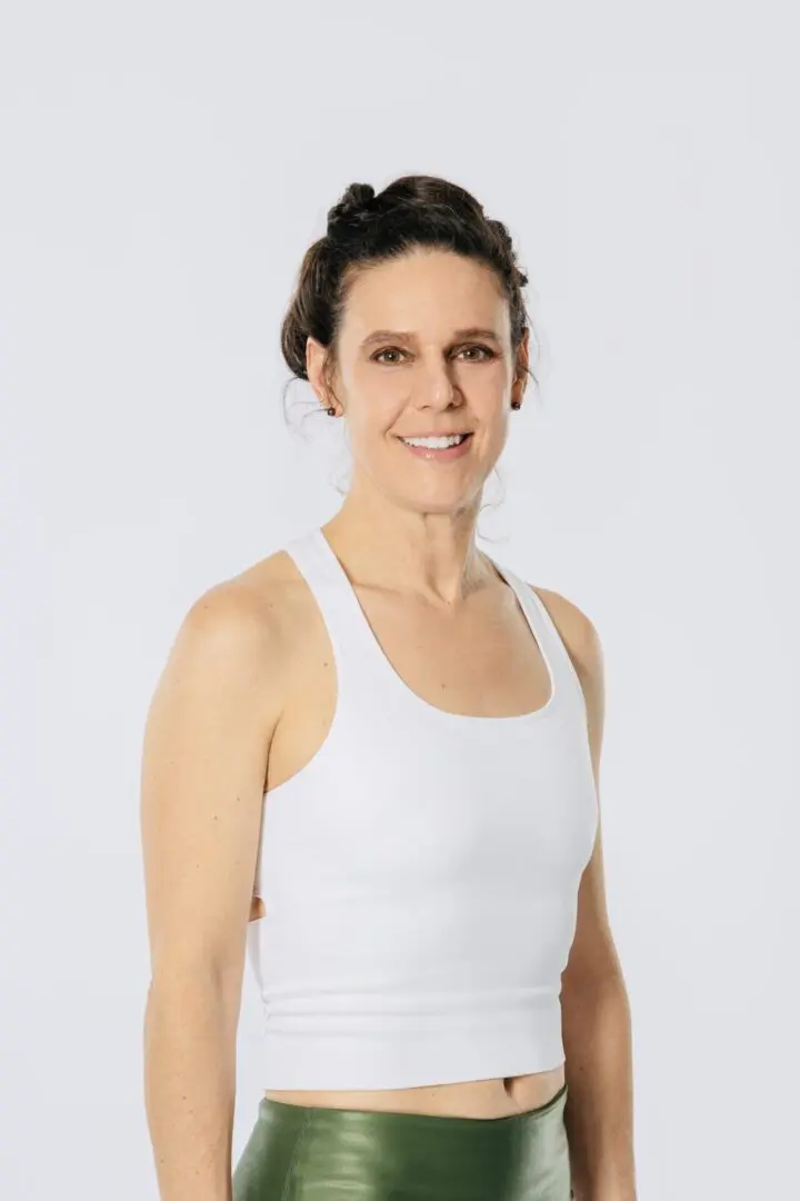 A woman in white tank top standing next to wall.